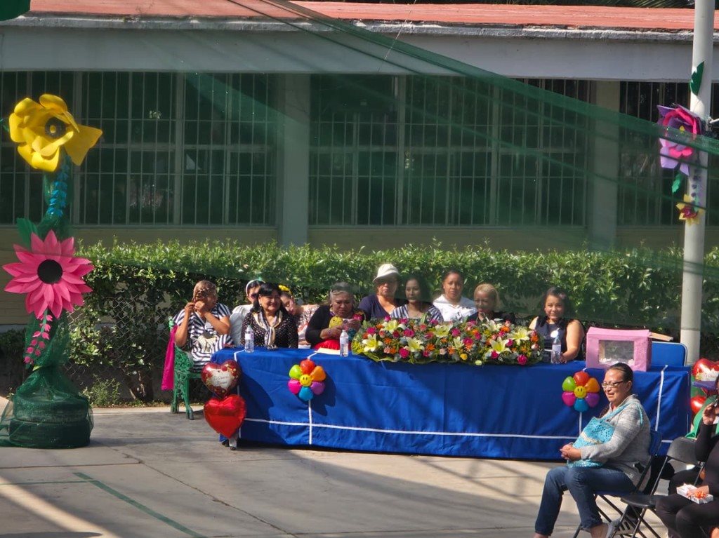 Mesa de honor decorada con flores y mamás de la comunidad escolar invitadas al evento